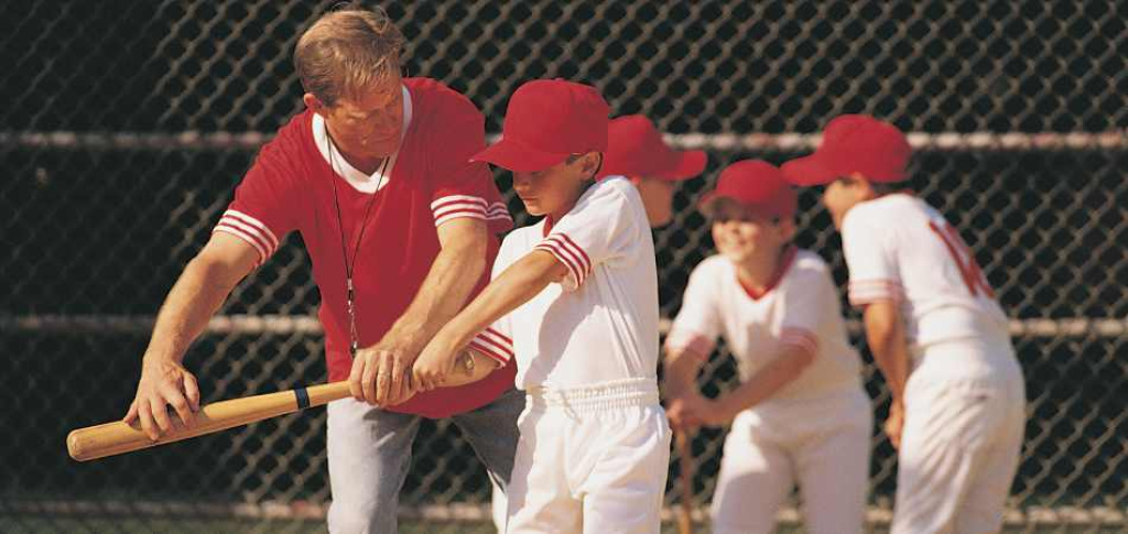 Baseball coach teaching athlete to swing.