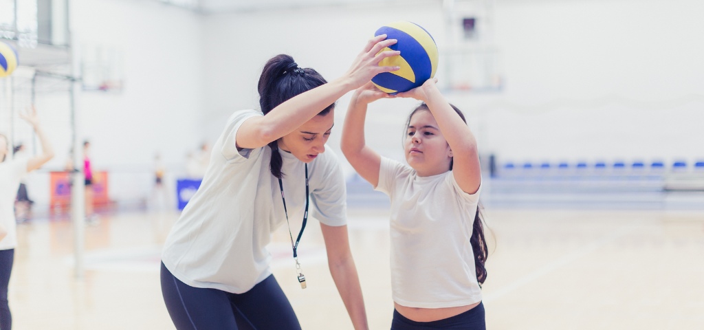 Volleyball coach helping youth player with serving form.