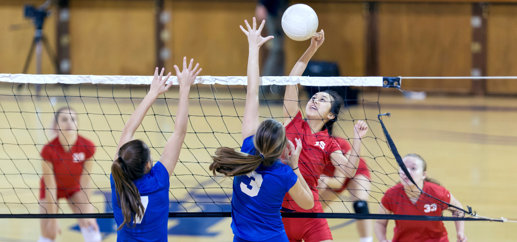 Volleyball player jumping above net to hit ball.