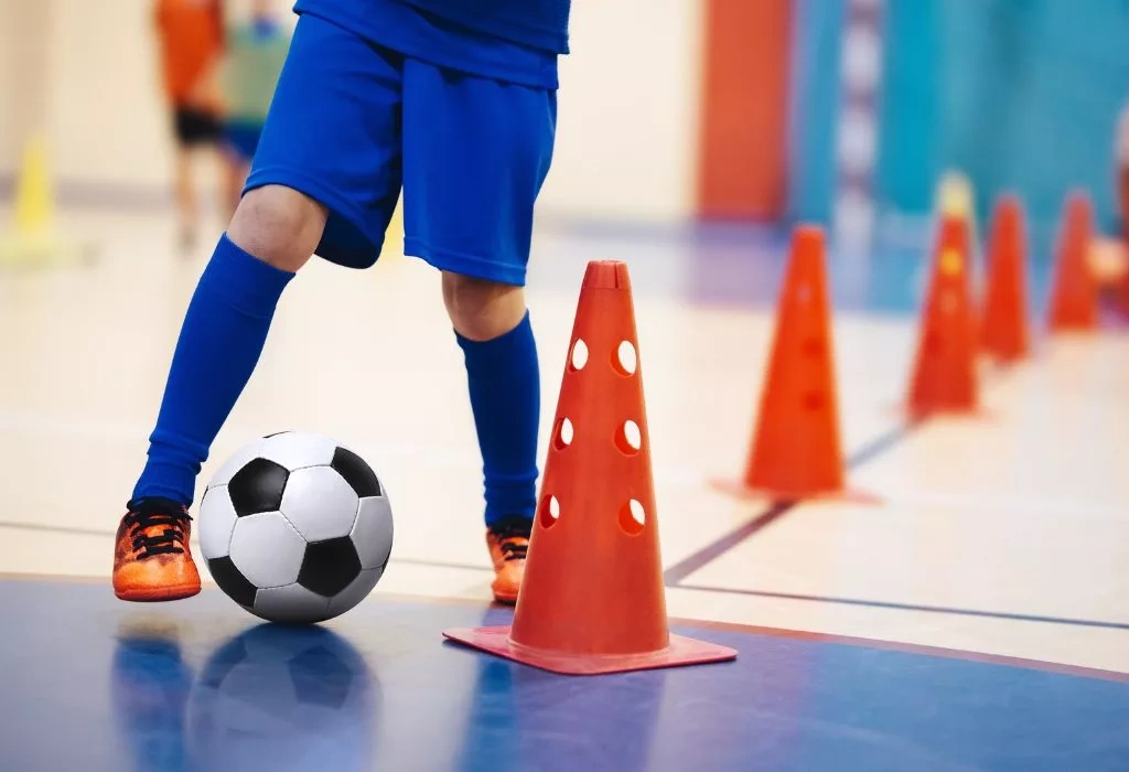 Soccer player dribbling ball through cones.