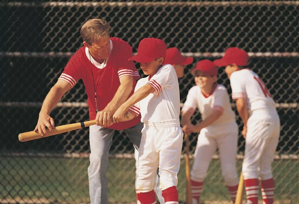Youth baseball coach instructing player to hit bat.