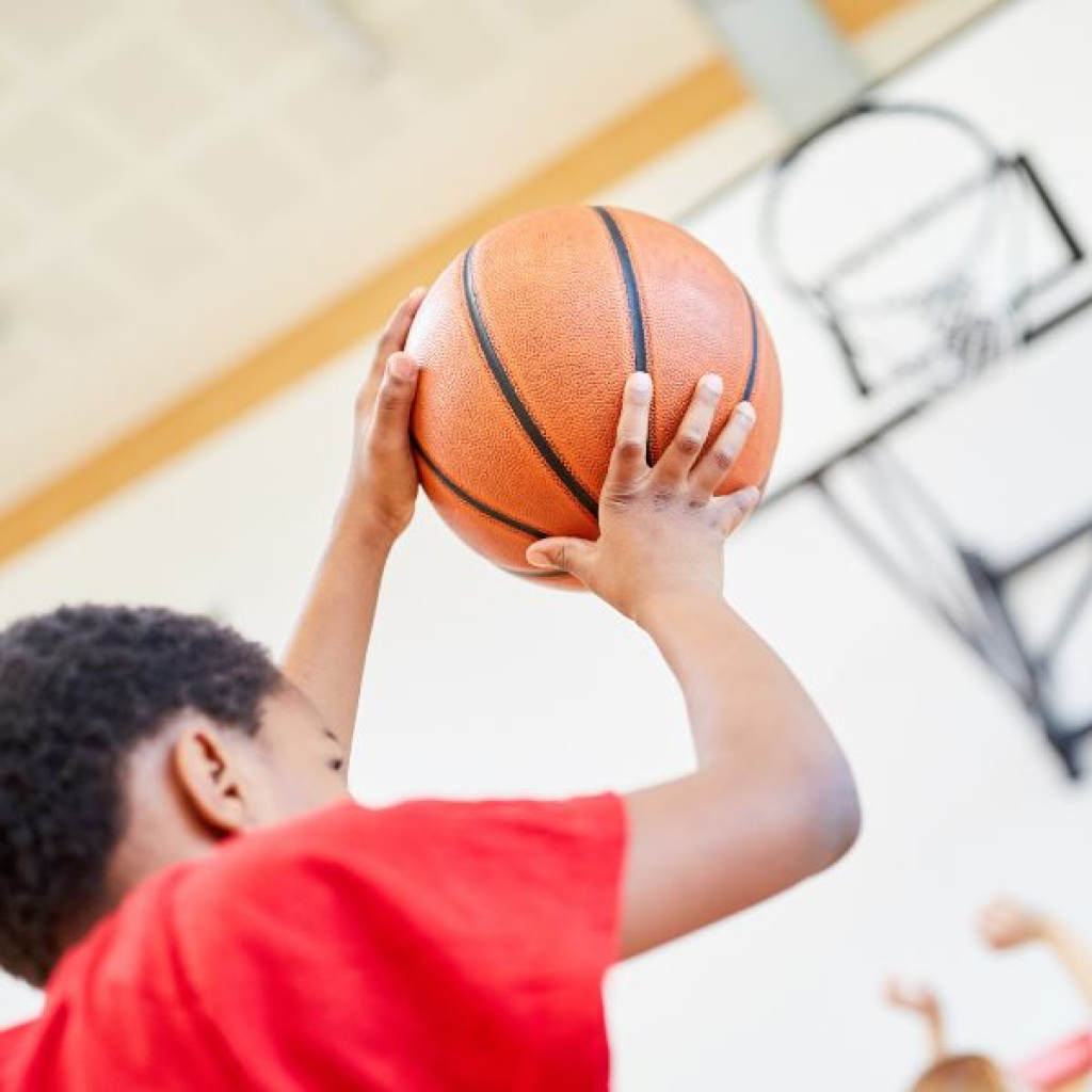 Young volleyball player under net with basketball.