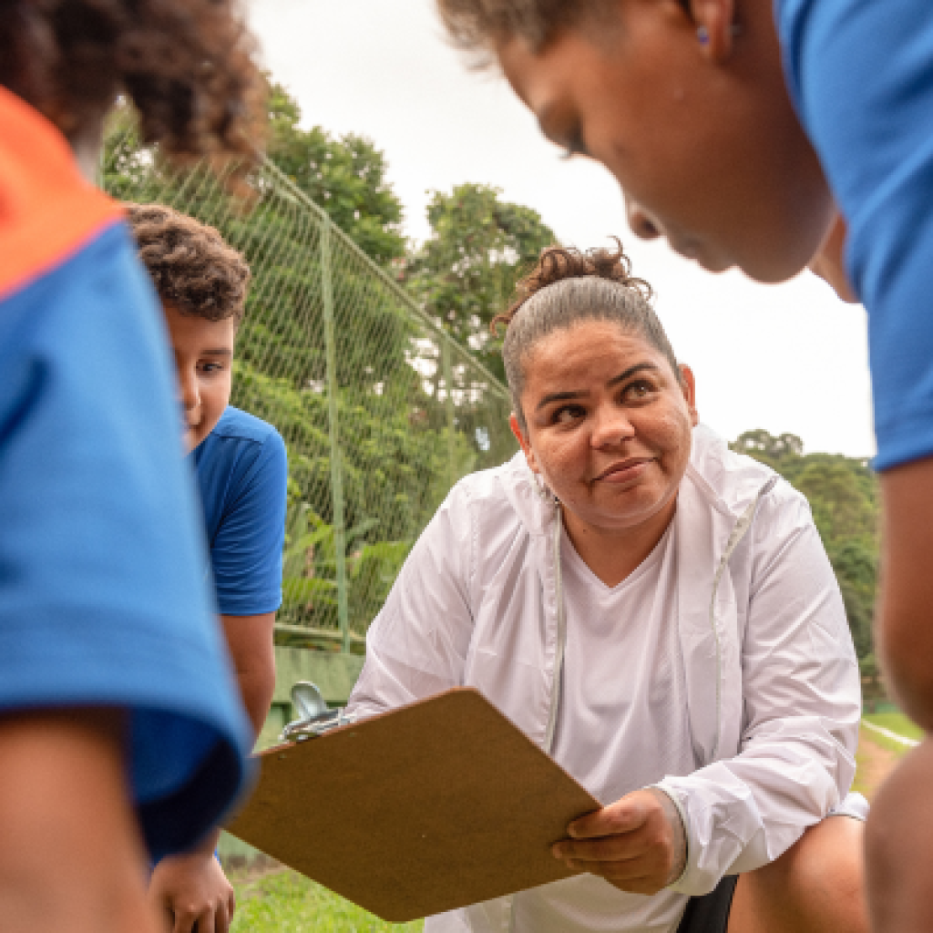 Coach with clipboard and athletes huddled around.